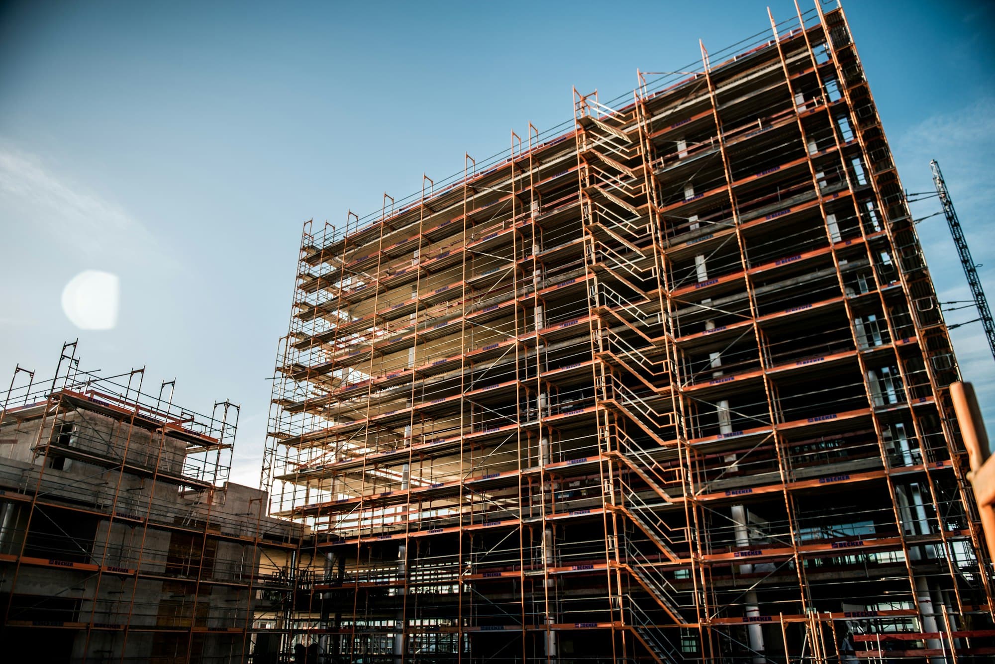 Multi-storey building fully wrapped in steel tube scaffolding against a blue sky