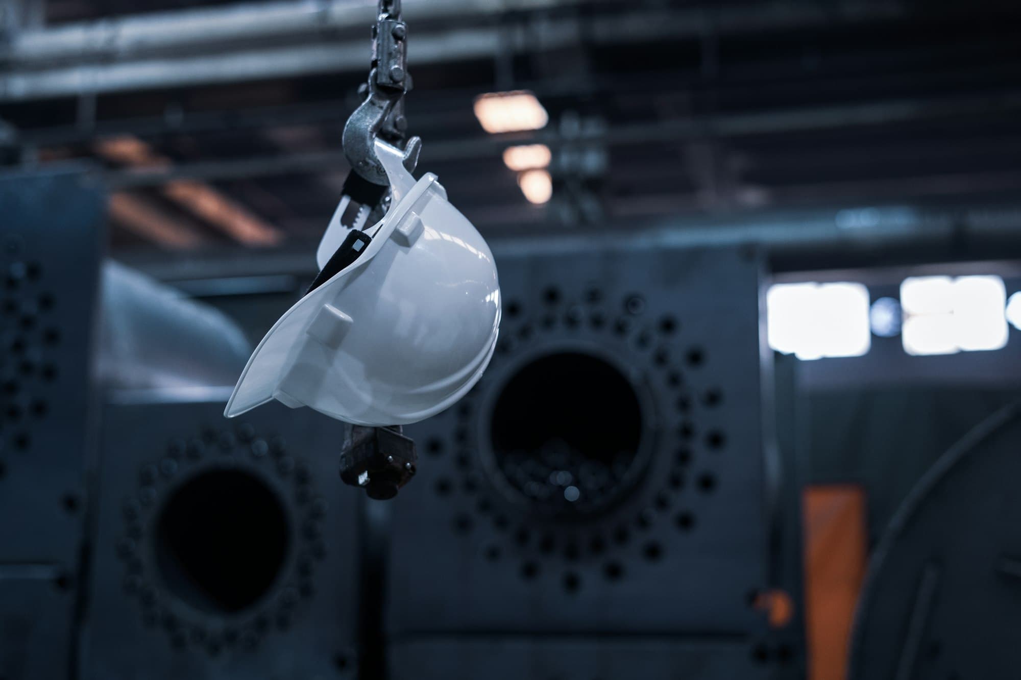 A white safety helmet hanging from a steel hook in a dark industrial building