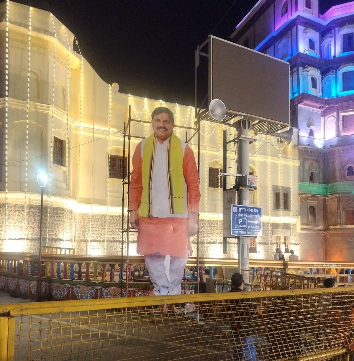 Giant cut-out standee held up by a scaffold frame behind it at Rajwada Chowk, Indore, at night