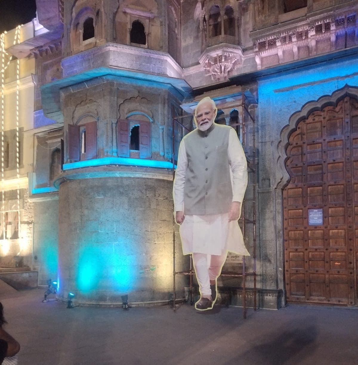 Tall cut-out standee in front of Rajwada Palace, Indore, with its supporting scaffold visible behind