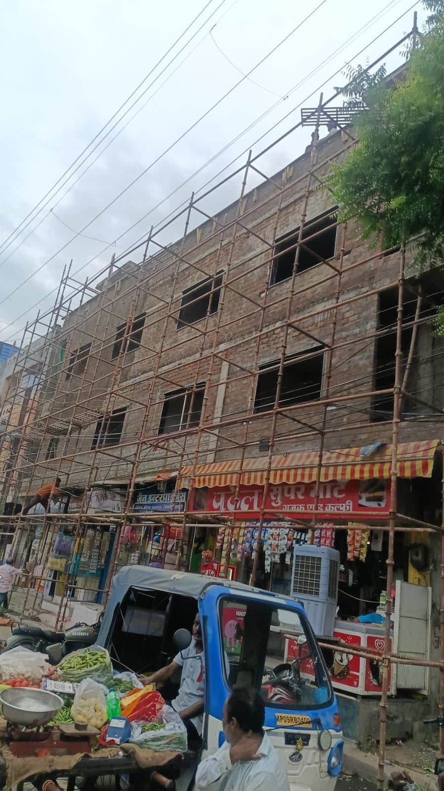 Scaffolders working on a brick building above shops on a busy market street